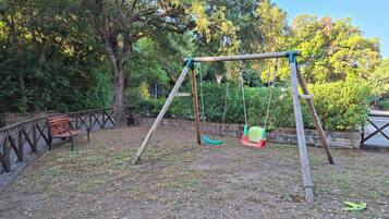 A swing set in a park with a bench and trees in the background.