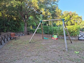En gunga i en park, med en bänk och träd i bakgrunden.