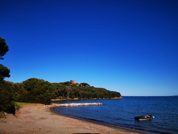 A beach with a boat, a rocky shoreline, and a castle on a hill.