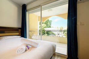 A hotel room with a bed, a rolled towel, and a view of a balcony with outdoor furniture. - Platinium 1 Apartment (Cannes)