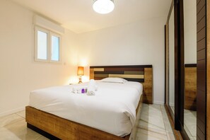 A hotel room with a wooden bed, a nightstand with a lamp, and a window with blinds. - Platinium 1 Apartment (Cannes)