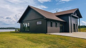 A two-story building with a dark exterior, a sloped roof, and a large window on the ground floor. - Modern Lakefront on Toledo Bend, 3BR • Sleeps 7 • Boat Launch & Amazing Views (Many)