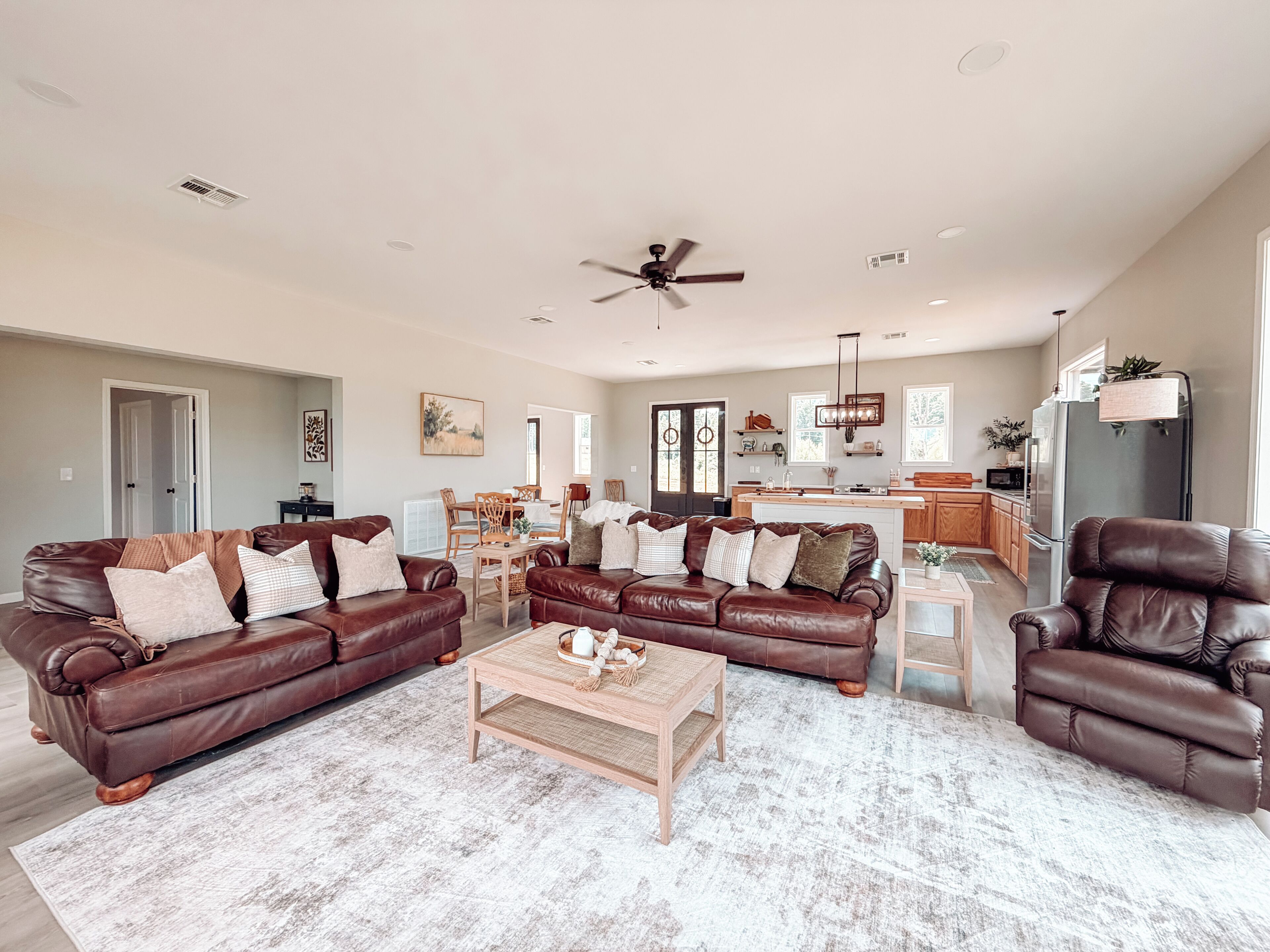 A spacious living room with leather sofas, a coffee table, and a ceiling fan.
