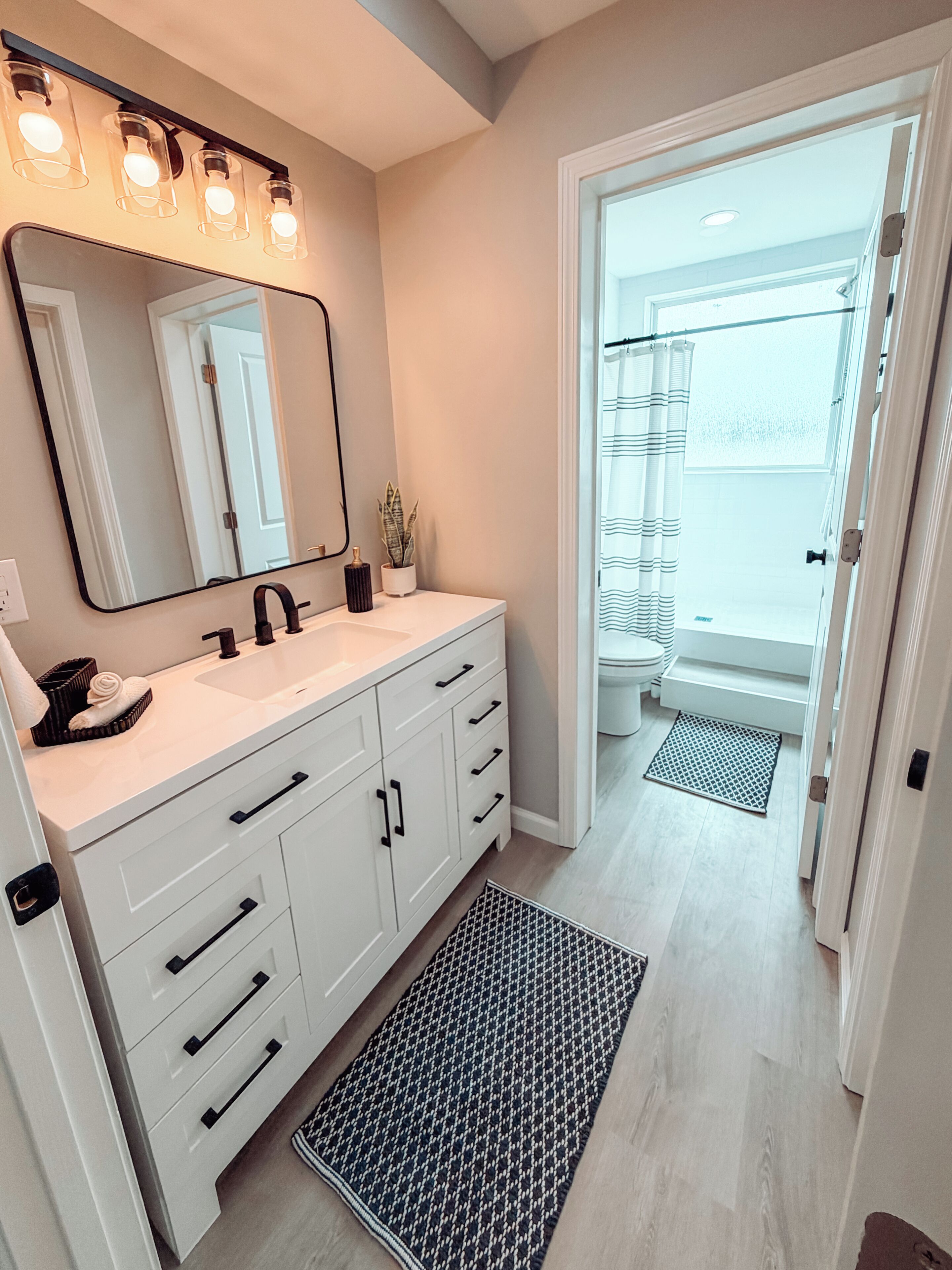 Une salle de bain avec un meuble-lavabo blanc, un grand miroir et un luminaire placé au-dessus du miroir.
