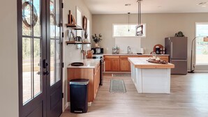 A modern kitchen with wooden cabinets, a central island, and a large window providing natural light. - Modern Lakefront on Toledo Bend, 3BR • Sleeps 7 • Boat Launch & Amazing Views (Many)