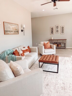 Ein Wohnzimmer mit Sofa, Sesseln, Hocker und Kamin mit Stauraum.