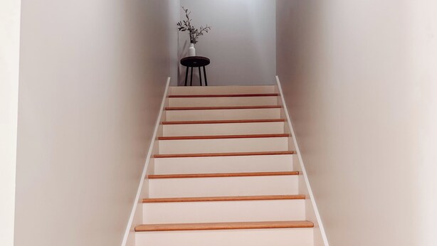 A staircase with wooden steps and white walls, leading to a room with a small table and a plant. - Modern Lakefront on Toledo Bend, 3BR • Sleeps 7 • Boat Launch & Amazing Views (Many)