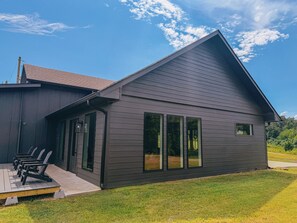 Une maison moderne avec une façade sombre, de grandes fenêtres et une terrasse équipée de chaises.