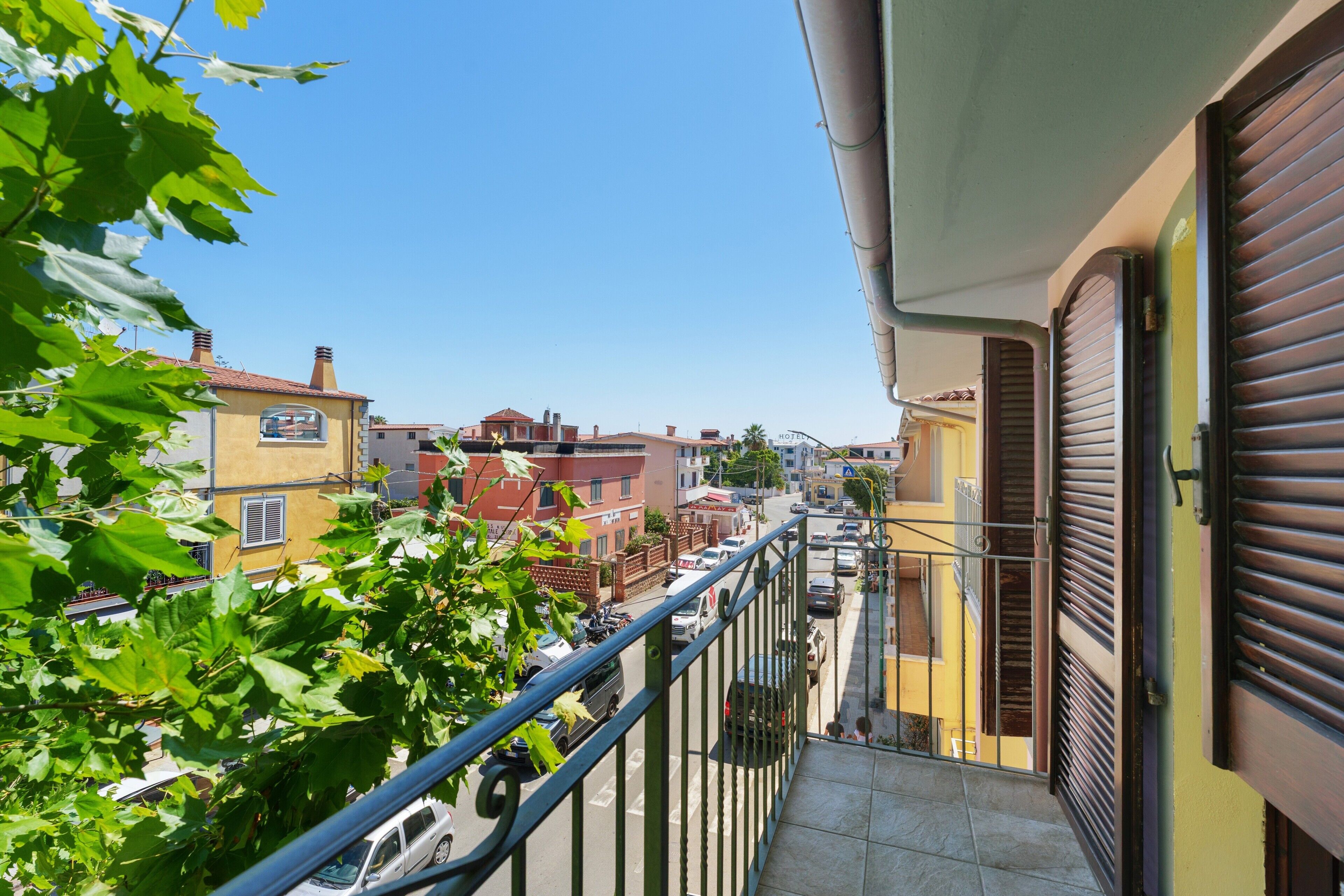 A balcony with a metal railing overlooking a street with parked cars and buildings.