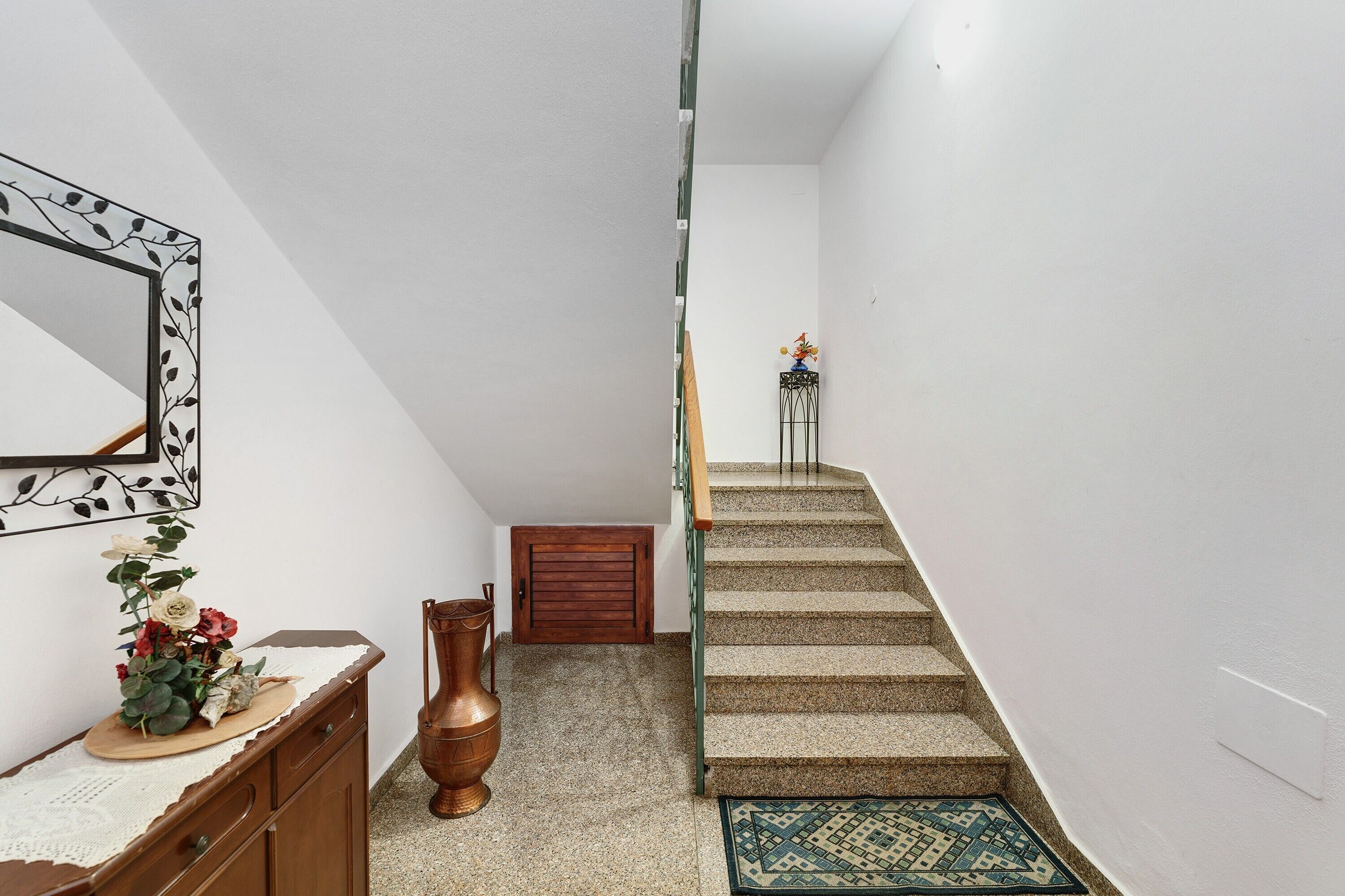 A staircase with a wooden handrail, a small table with a vase of flowers, and a decorative mirror on the wall.