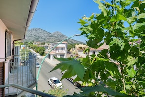 Un balcó amb vista a un carrer, edificis i muntanyes al fons.