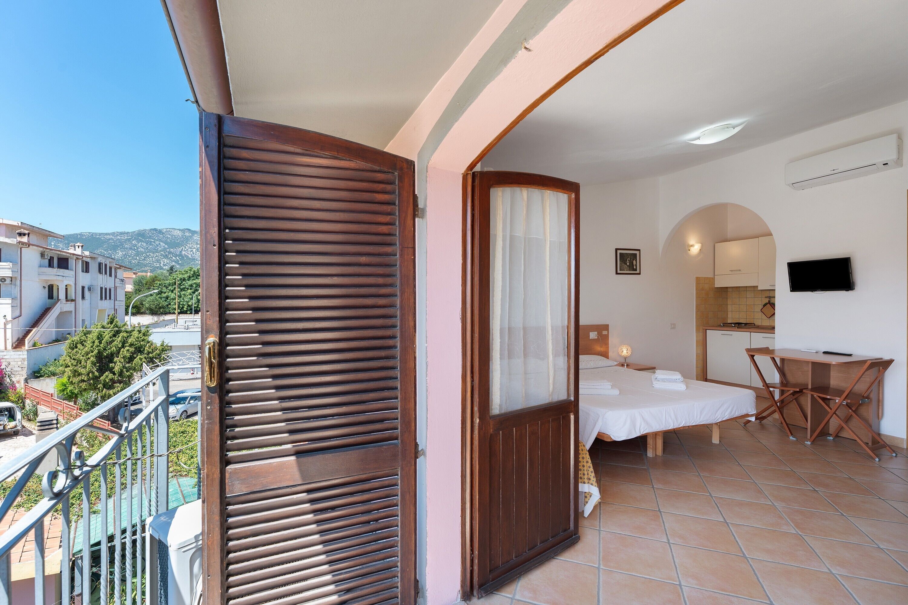 A balcony with a wooden door, a bed, a desk, and a TV.
