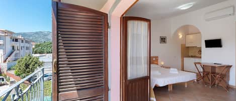 A balcony with a wooden door, a bed, a desk, and a TV.