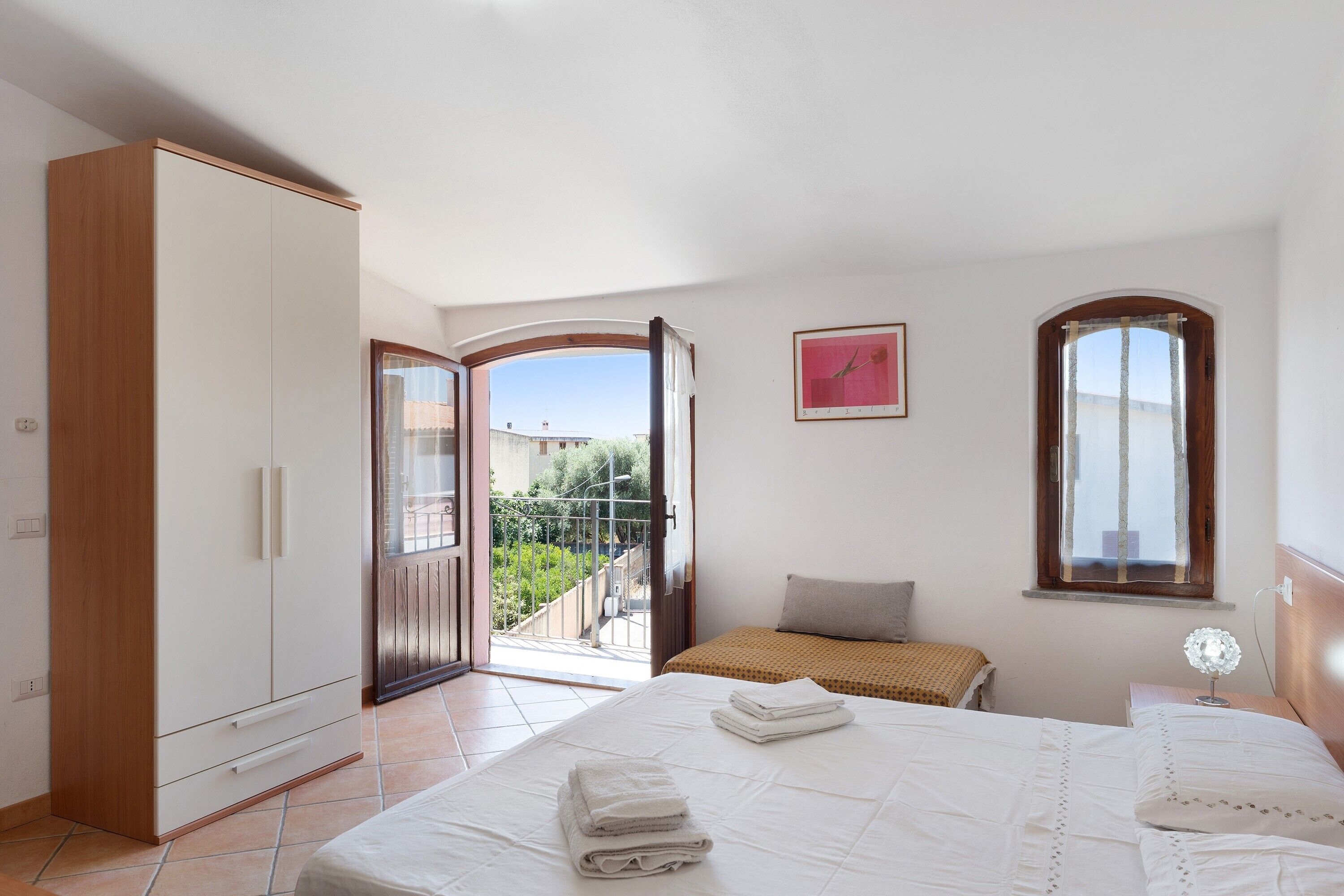 A bedroom with a bed, a wardrobe, a window, and a door leading to an outdoor area.