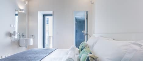 A hotel room with a bed, a bedside table, a mirror, a window, and a door.