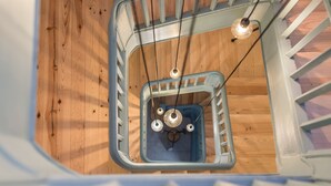 A wooden floor with a metal staircase railing and a hanging light fixture. - Casa do Ofício - Boilermaker 5 by Hosty (Porto)