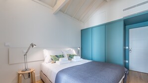 A bedroom with a bed, bedside lamps, a wooden nightstand, a teal wardrobe, and a white door. - Casa do Ofício - Boilermaker 5 by Hosty (Porto)