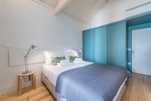 A bedroom with a bed, bedside lamps, a wooden nightstand, a teal wardrobe, and a white door. - Casa do Ofício - Boilermaker 5 by Hosty (Porto)