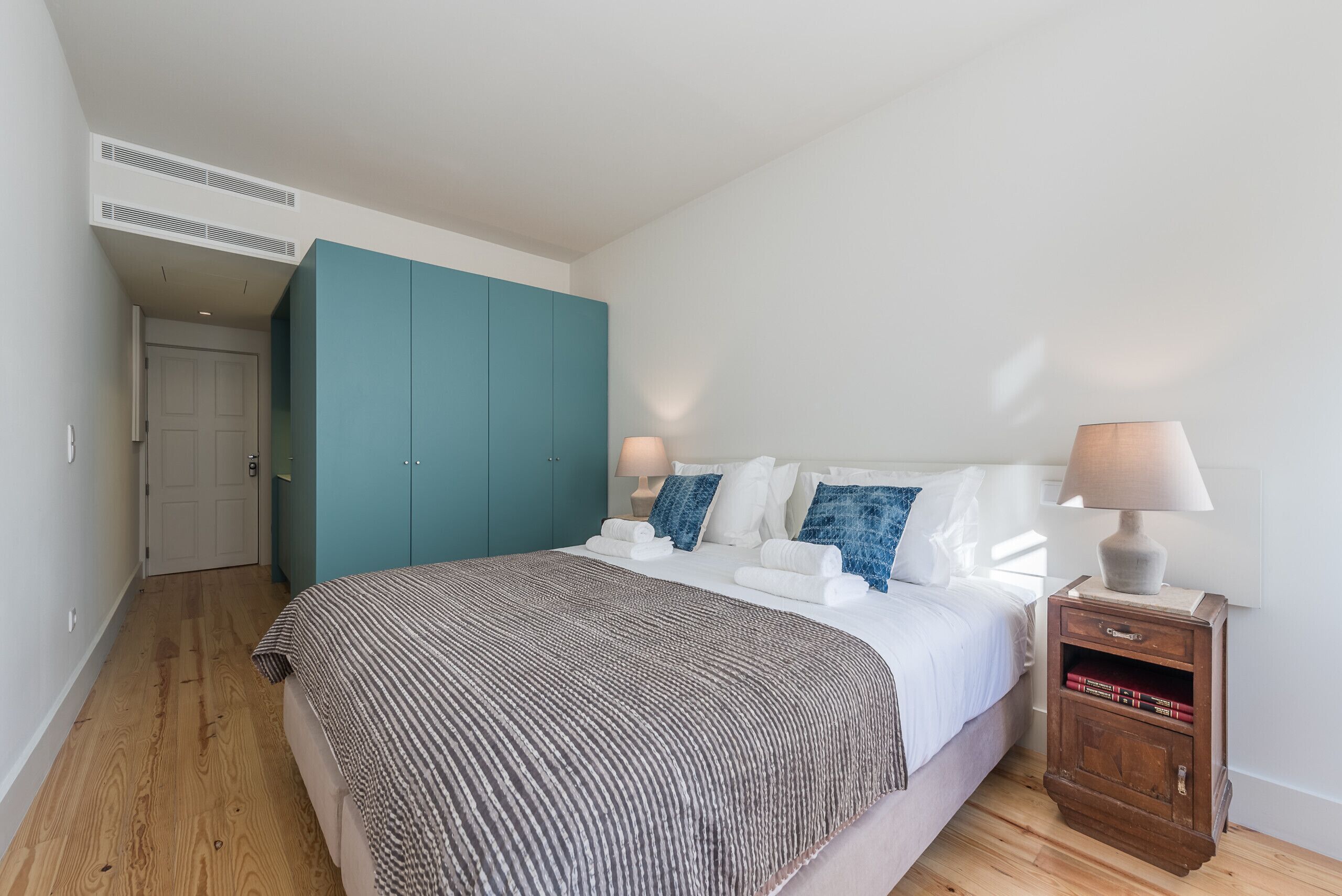 Un dormitorio con una cama, una mesita de noche, un armario color esmeralda y una puerta.