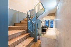 Eine Treppe mit Holzboden und blauen Geländern führt zu einer erhöhten Wohnfläche mit Blick nach außen.