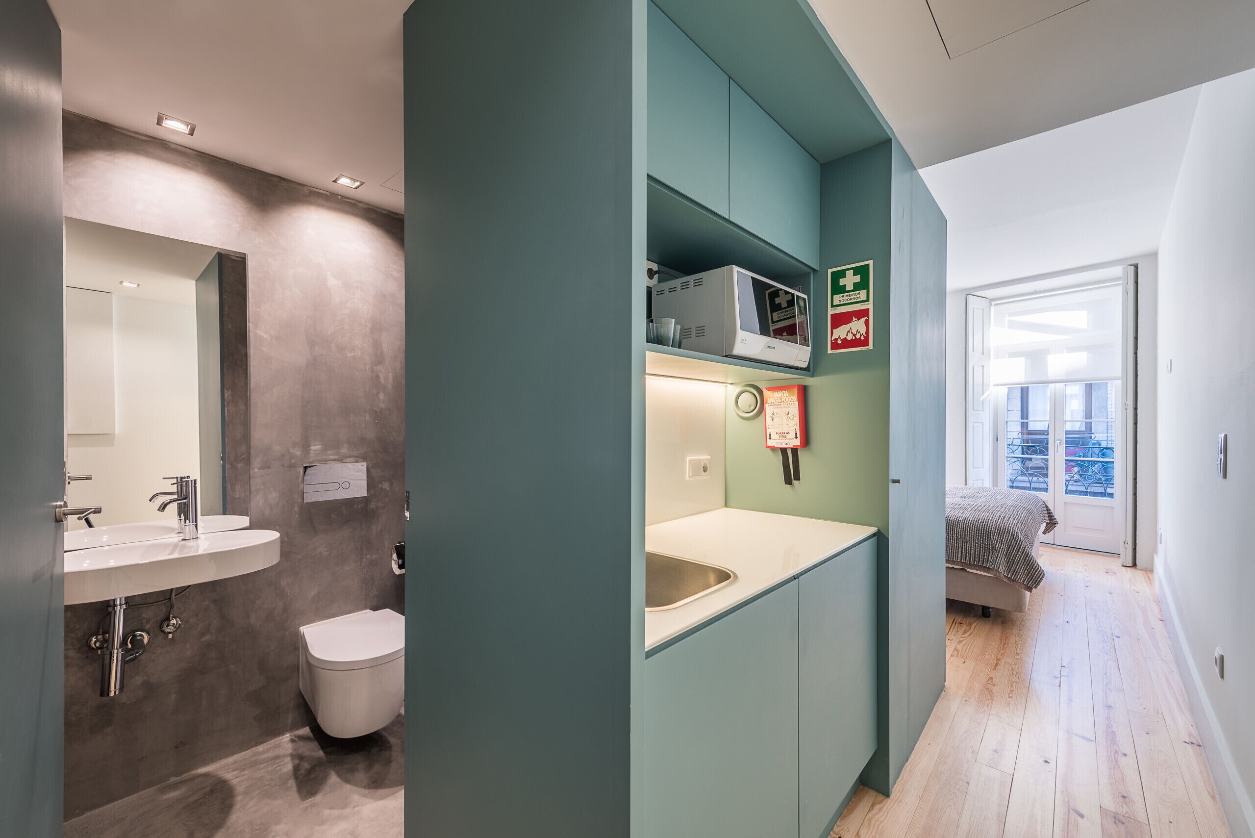 Et moderne badeværelse med vask, spejl og toilet. Der er en hylde med en mikroovn og et førstehjælpskasse. En brandalarm er monteret på væggen.