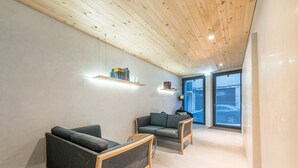En moderne stue med to grå sofaer, træbjælker i loftet og et stort vindue med udsigt til en bil.