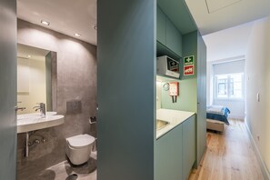 Een moderne badkamer met een wastafel, toilet en douche. Een bed is zichtbaar in de aangrenzende kamer.