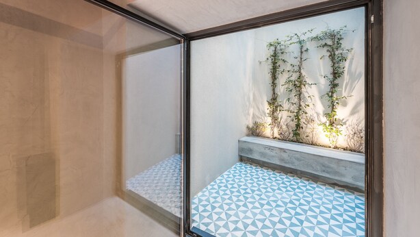 A corner of a room with a tiled floor, a concrete bench, and a wall with climbing plants. - Casa do Ofício - Boilermaker 1 by Hosty (Porto)