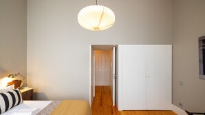 A bedroom with a bed, bedside table, lamp, and a hanging light fixture. - Casa do Ofício - Bookseller 3 by Hosty (Porto)