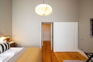 A bedroom with a bed, bedside table, lamp, and a hanging light fixture. - Casa do Ofício - Bookseller 3 by Hosty (Porto)