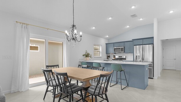 Una cocina moderna con una isla central, un comedor con mesa y sillas de madera, y una lámpara de araña.