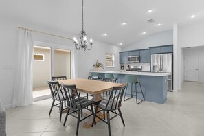 A modern kitchen with a central island, a dining area with a wooden table and chairs, and a chandelier. - Welcome to the Elegant 3/2 Courtyard Villa in the Village of Hawkins (The Villages)