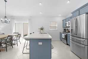Een moderne keuken met een centraal eiland, roestvrijstalen apparatuur en een eethoek met een kroonluchter.