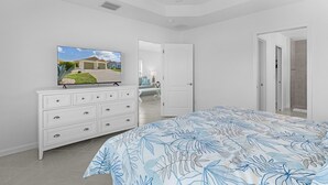 Un dormitorio con cama, cómoda, televisor y puerta que da a otra habitación.