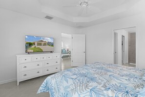 A bedroom with a bed, dresser, TV, and a door leading to another room. - Welcome to the Elegant 3/2 Courtyard Villa in the Village of Hawkins (The Villages)