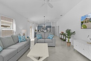 A modern living room with a grey sofa, a coffee table, and a kitchen in the background. - Welcome to the Elegant 3/2 Courtyard Villa in the Village of Hawkins (The Villages)