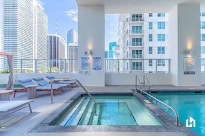Un espace piscine aménagé sur le toit, avec des chaises longues et une vue sur les bâtiments de la ville.