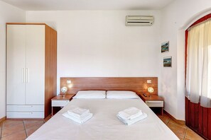 Ein Hotelzimmer mit einem Bett, zwei Nachttischen, einem Kleiderschrank, einer Klimaanlage und einem Fenster mit Vorhängen.