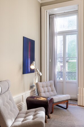 A room with a large window, a chair, a sofa, and a lamp. - Casa do Ofício - Bookseller 2 by Hosty (Porto)