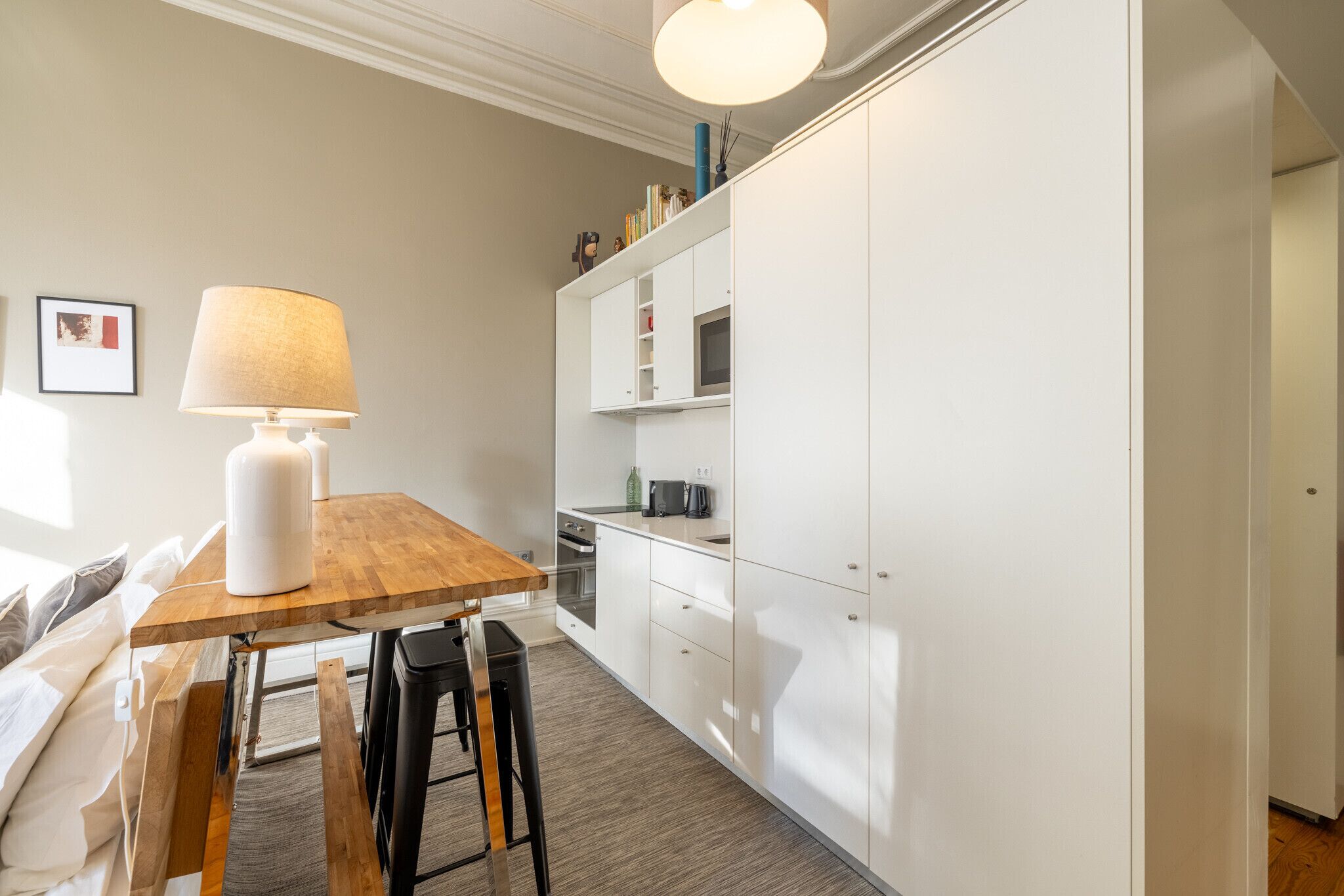 A compact kitchen with white cabinets, a wooden table, and a lamp.