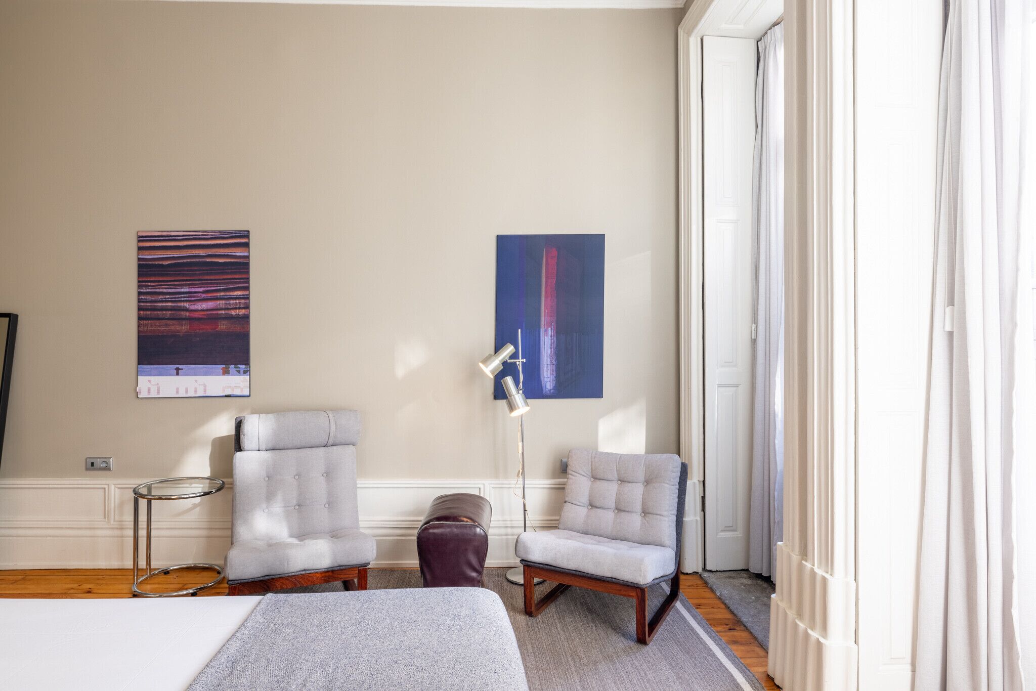 A room with two armchairs, a floor lamp, a bench, and two abstract paintings on the wall.