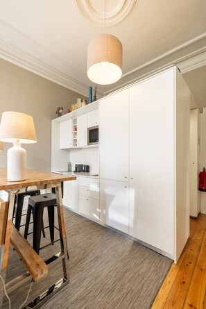 A modern kitchen with white cabinetry, a wooden table, and a hanging light fixture. - Casa do Ofício - Bookseller 2 by Hosty (Porto)