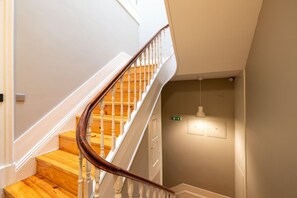 A staircase with wooden steps and white balusters, a light switch, and an emergency exit sign. - Casa do Ofício - Bookseller 4 by Hosty (Porto)