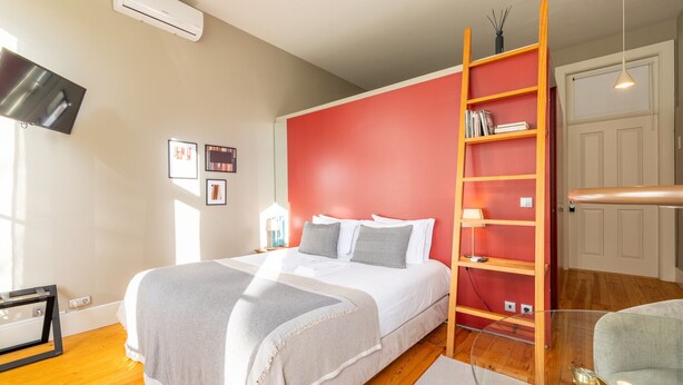 A bedroom with a bed, a red wall, a bookshelf, a TV, and a window. - Casa do Ofício - Bookseller 4 by Hosty (Porto)