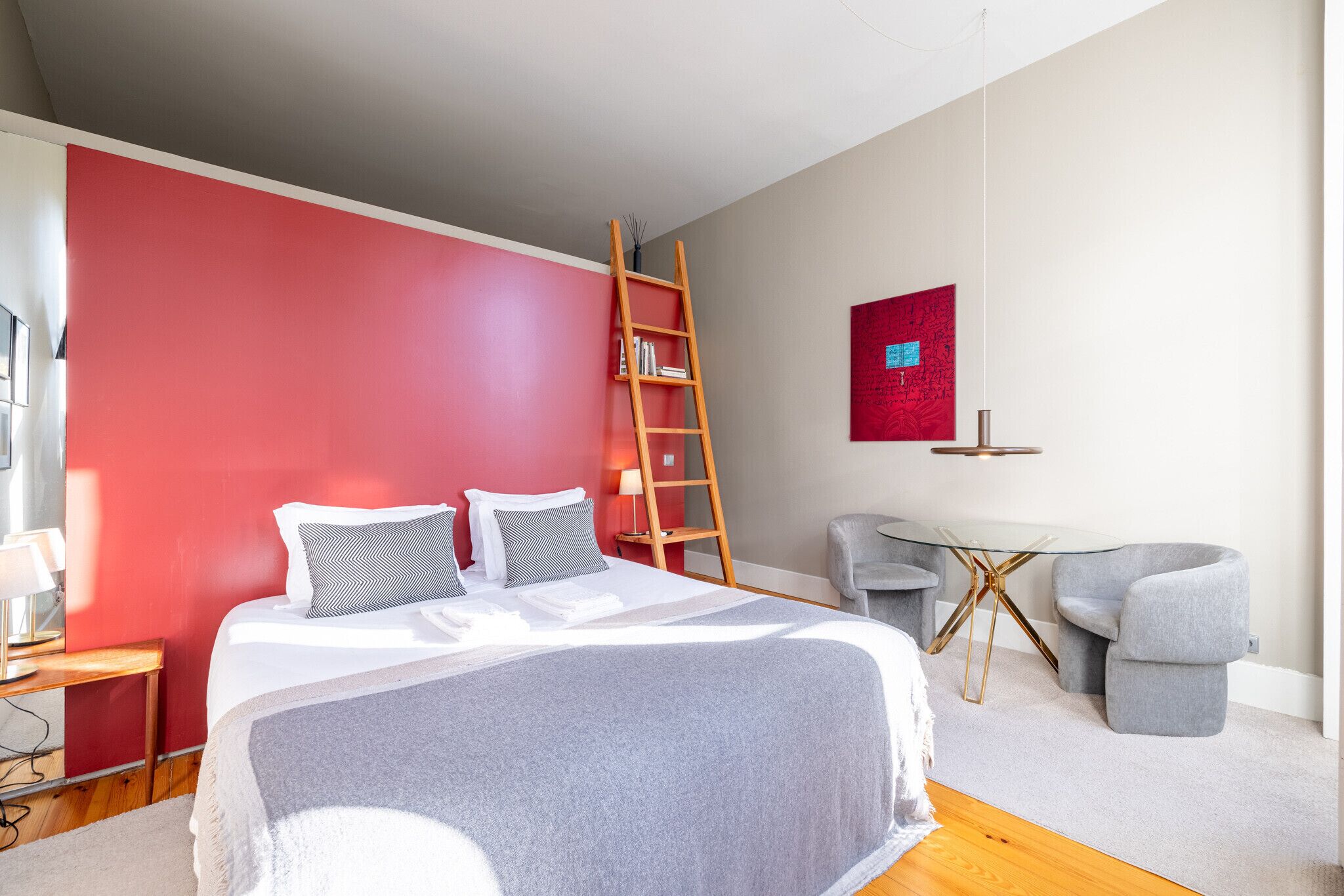 Ein Schlafzimmer mit einem Bett, einem Schreibtisch, einem Stuhl, einer Leiter und einem Wandbild.