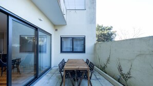 A patio with a wooden table and chairs, a sliding glass door, and a white wall with a window. - Casa do Ofício - Galerista by Hosty (Porto)
