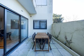 A patio with a wooden table and chairs, a sliding glass door, and a white wall with a window. - Casa do Ofício - Galerista by Hosty (Porto)