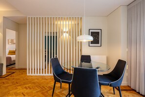 A modern dining area with a glass table and blue chairs, a white partition, and a framed artwork on the wall. - Casa do Ofício - Galerista by Hosty (Porto)