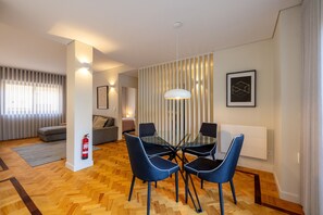 A modern living room with a sofa, a dining table with chairs, a fire extinguisher, and a radiator. - Casa do Ofício - Galerista by Hosty (Porto)