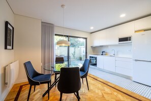 A modern kitchen with white cabinets, a microwave, and a Samsung refrigerator. There is a dining area with a glass table and two chairs. - Casa do Ofício - Galerista by Hosty (Porto)